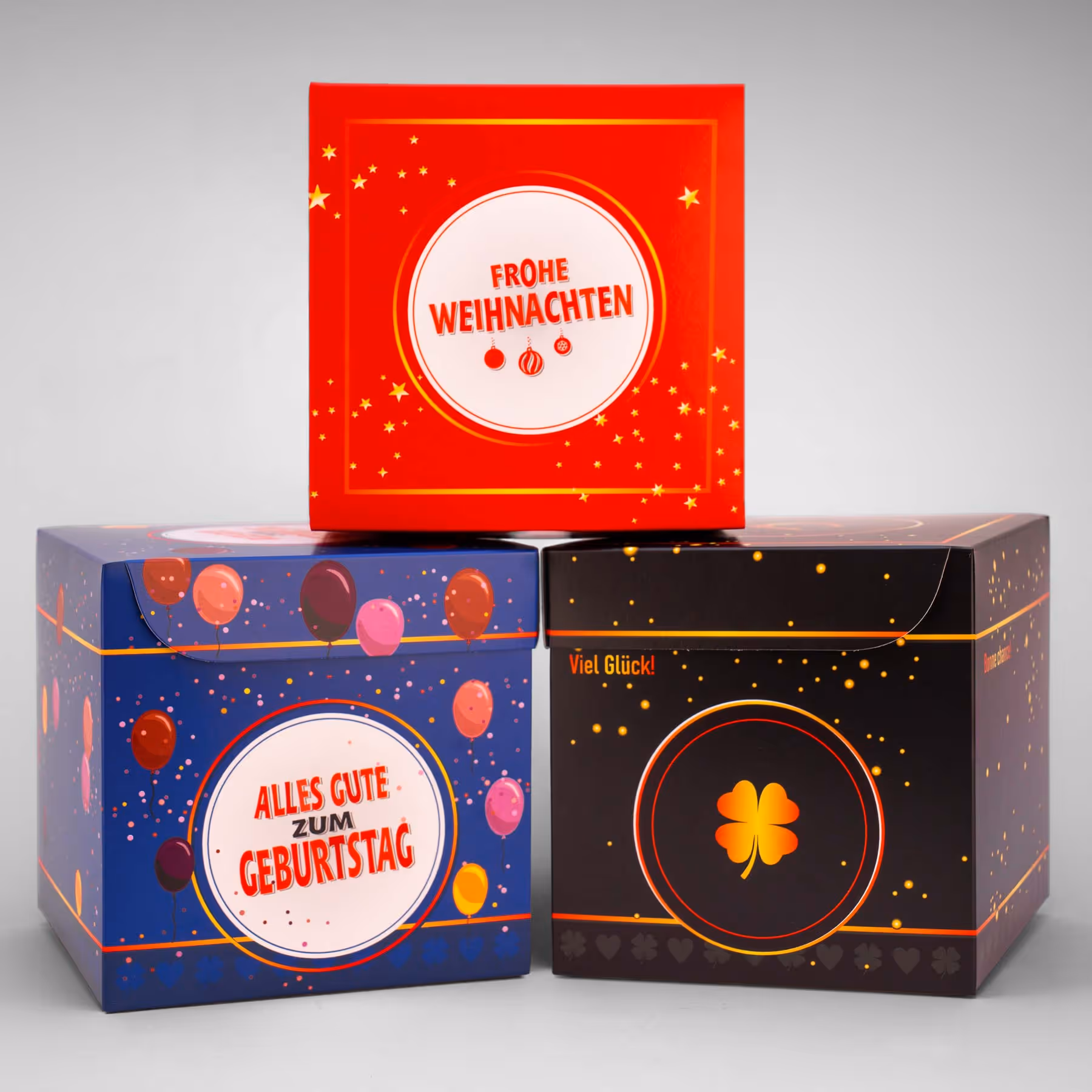 Drei farbenfrohe Geschenkboxen von KALO DORO – festliche Faltschachteln in Rot, Blau und Schwarz, gefertigt mit hochwertiger Veredelung von backesDruck.