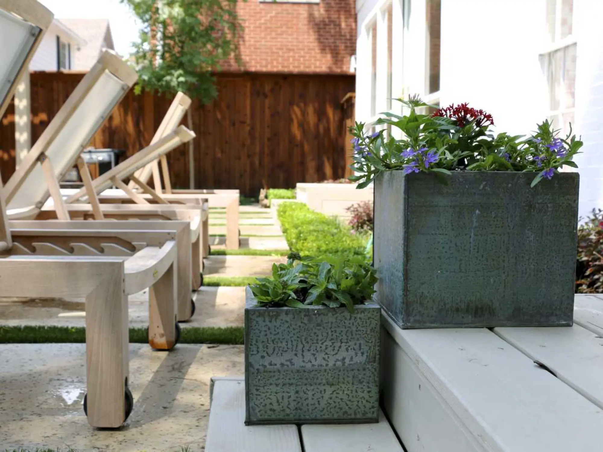 A small garden featuring a wooden bench beside a metal planter filled with vibrant flowers.