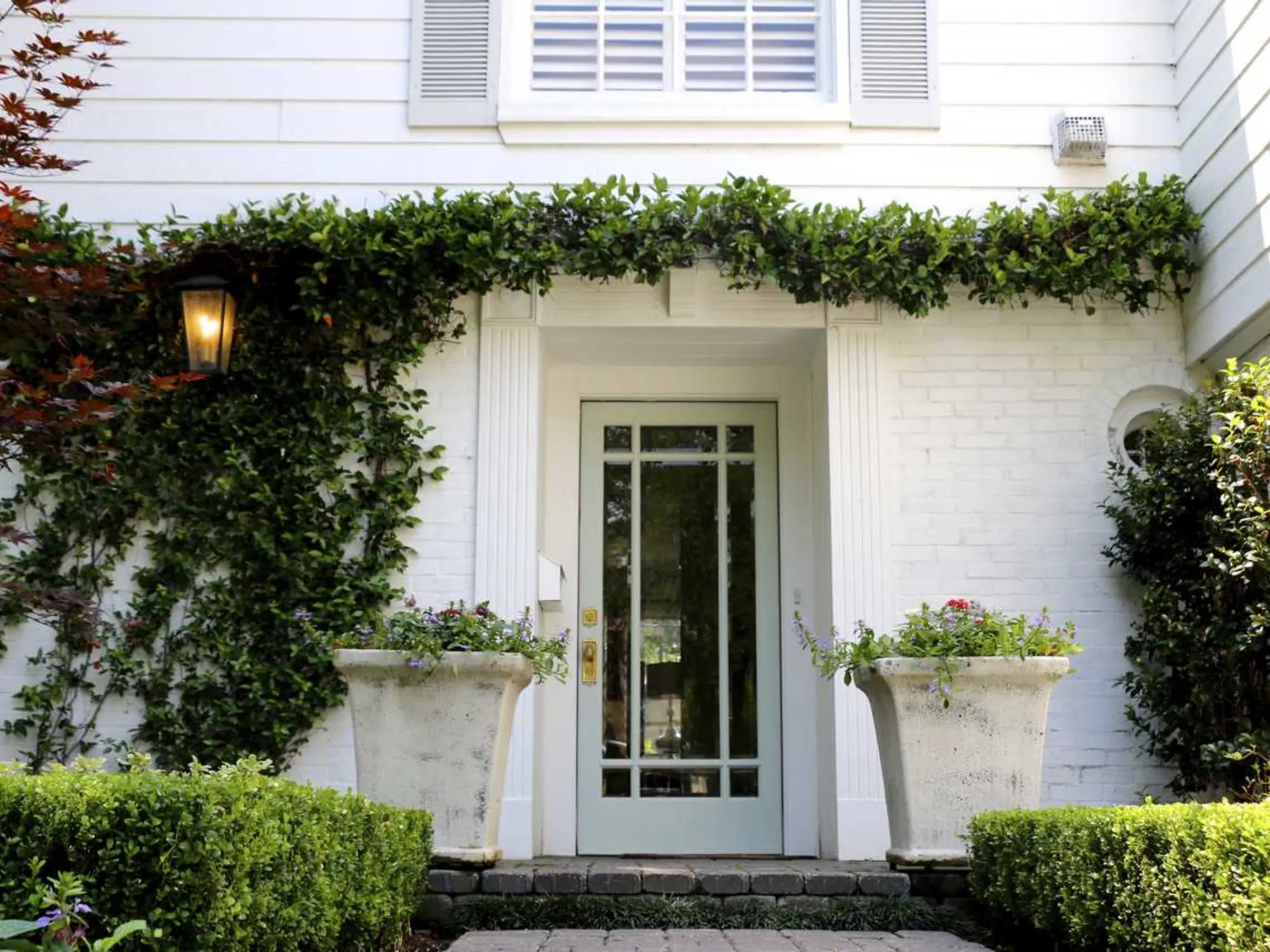 A white house featuring a door and a lush garden surrounding it, showcasing a serene outdoor space.