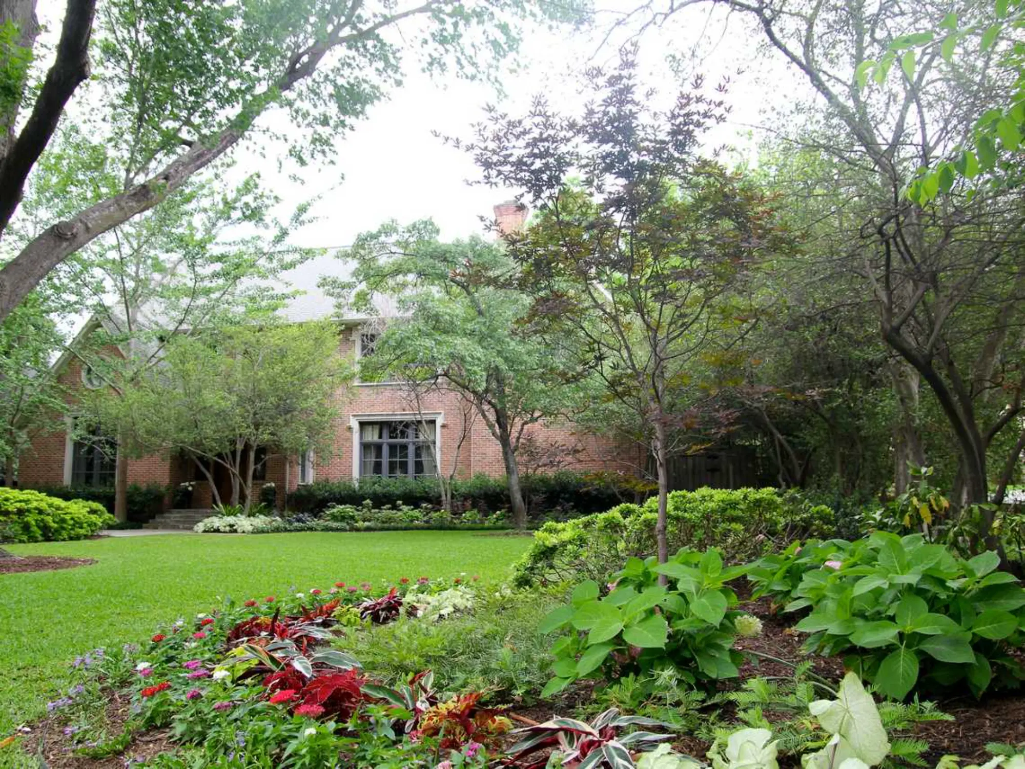 A vibrant garden filled with colorful flowers and lush shrubs, beautifully framing a charming house in the background.