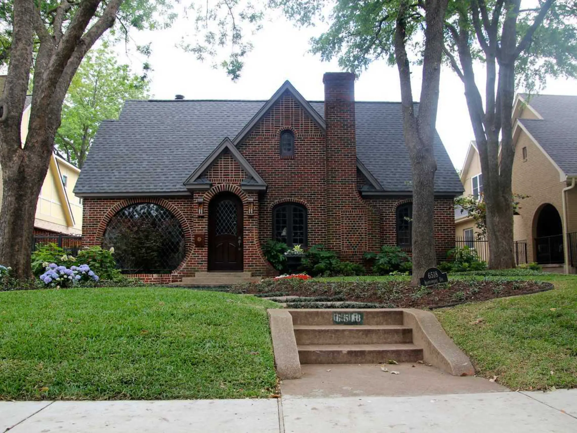 A brick house stands proudly with a large tree providing shade in front of it.
