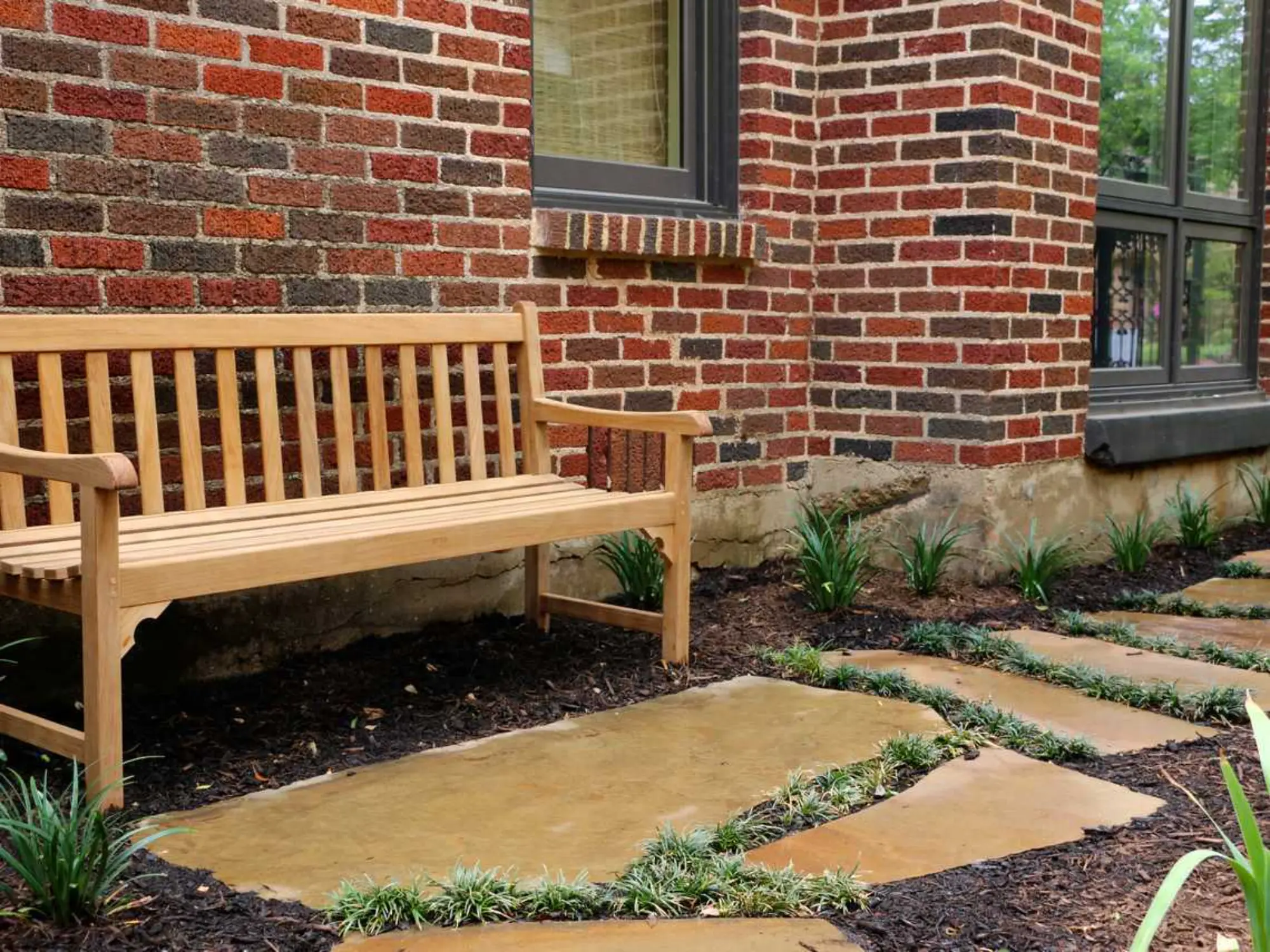 A wooden bench positioned in front of a rustic brick building, inviting relaxation in a charming setting.