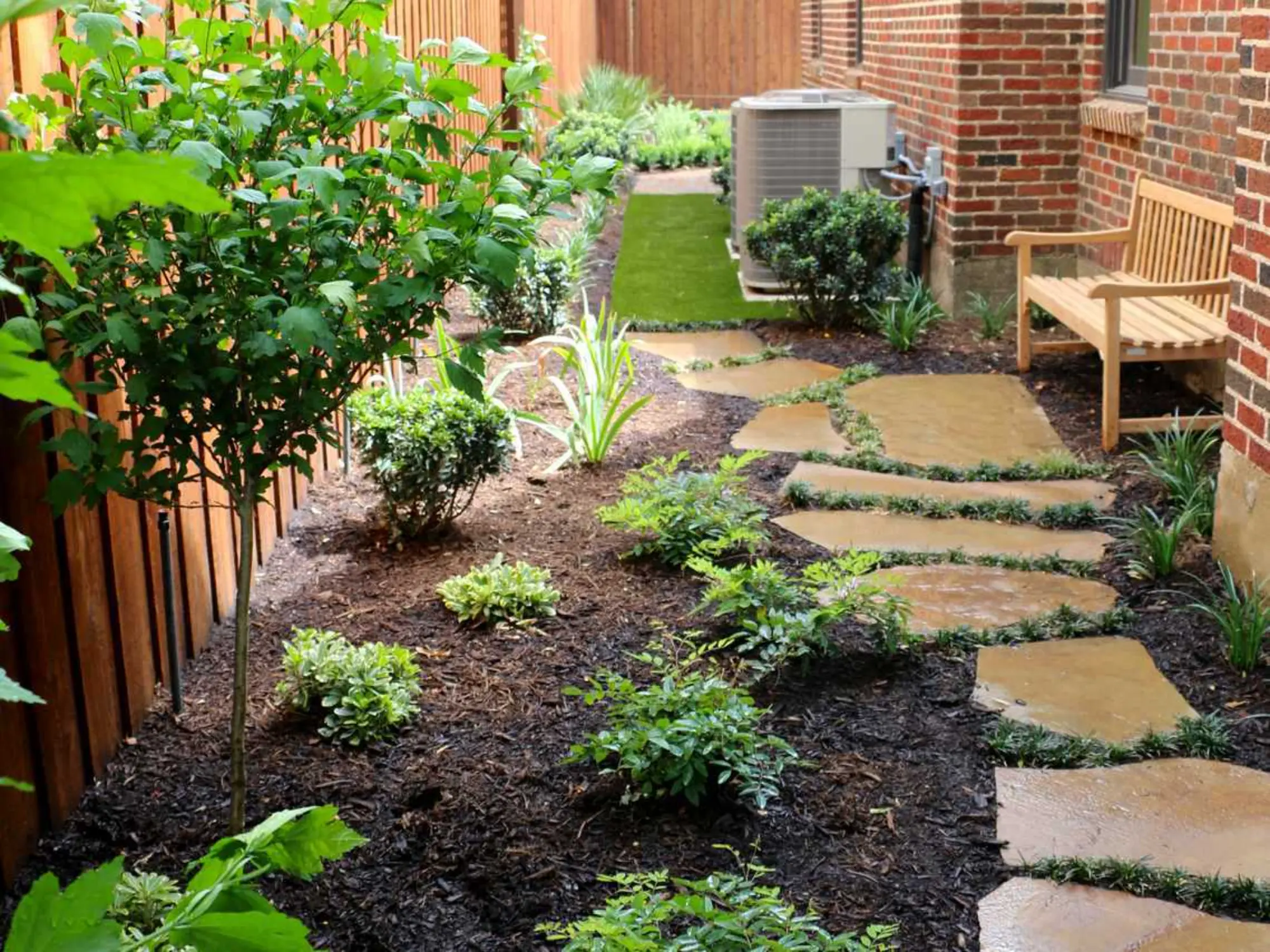 A charming backyard garden showcasing a stone path and a bench, inviting relaxation amidst blooming flowers.