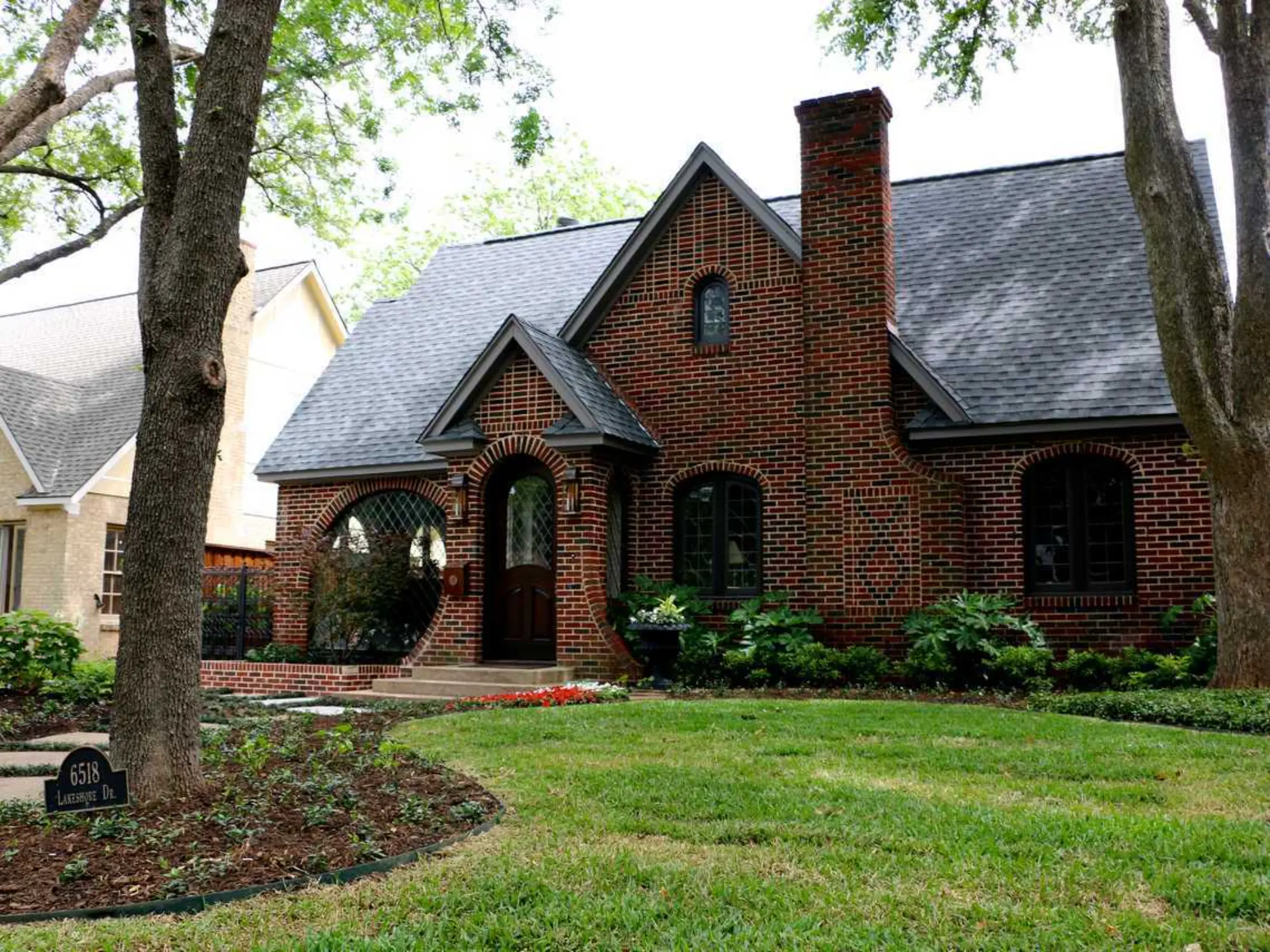 A cozy brick house is framed by a vibrant tree in front, enhancing the home's warm and welcoming appearance.