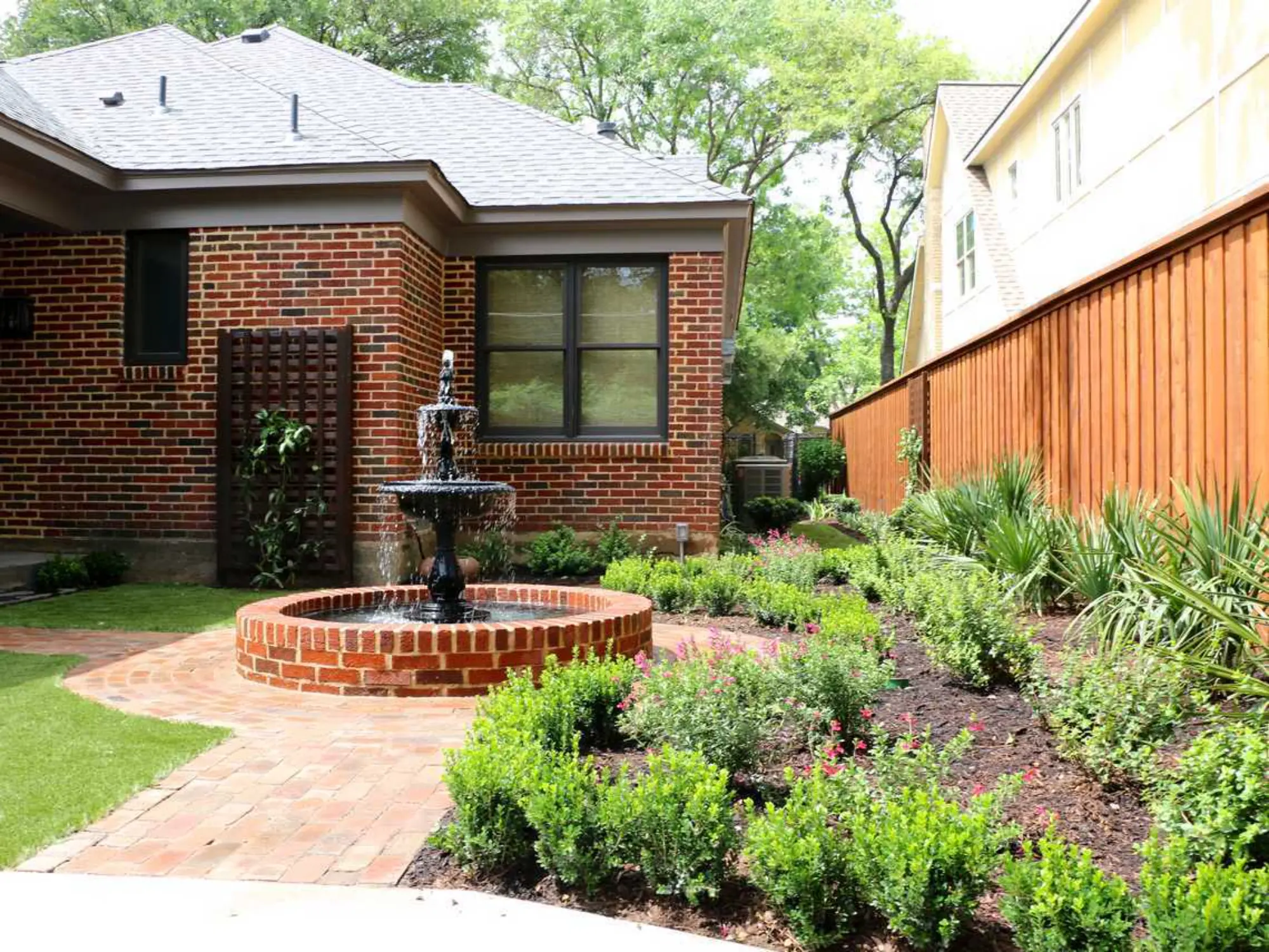 A brick patio featuring a fountain surrounded by a small, lush garden, creating a serene outdoor space.