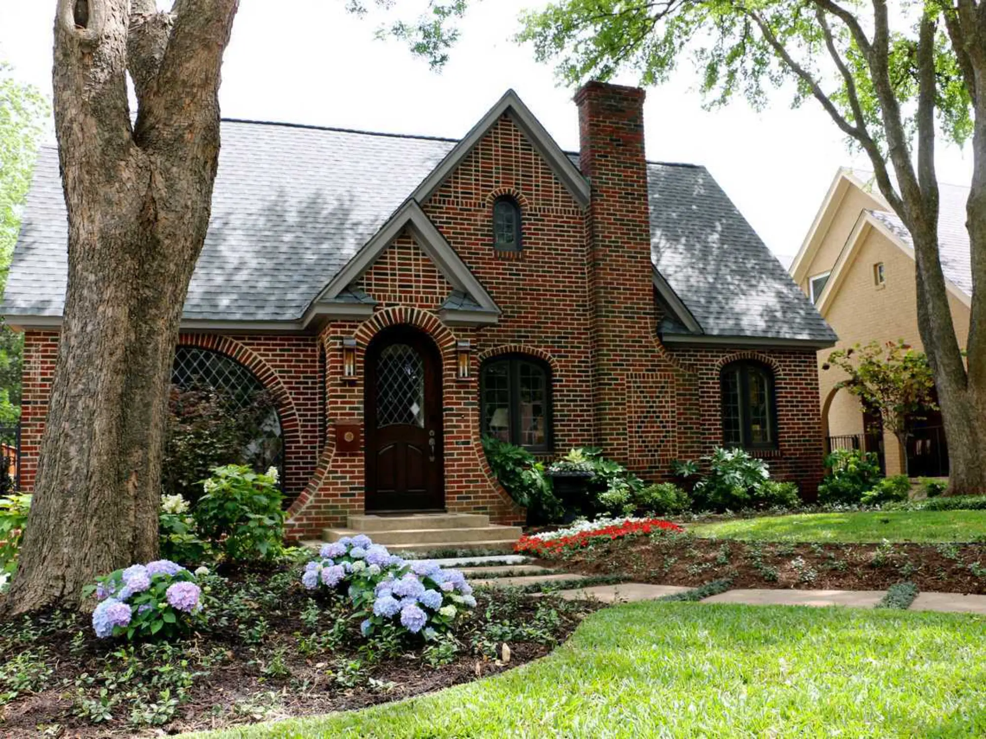 A brick house stands proudly with a lush green tree in front, creating a charming and inviting scene.