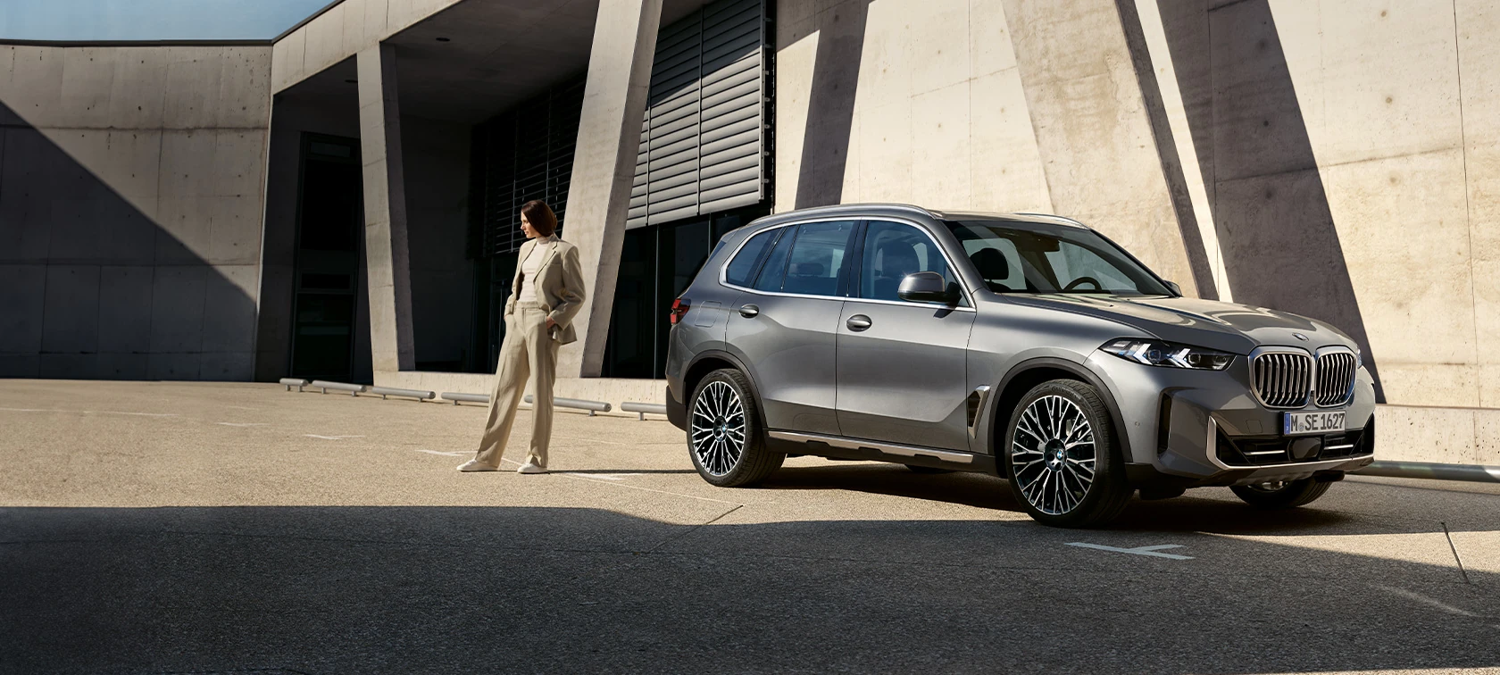 BMW X5  vor moderner Architektur mit einer Frau davor – Eleganz und Innovation im Autohaus BMW Köhler in Karlstadt