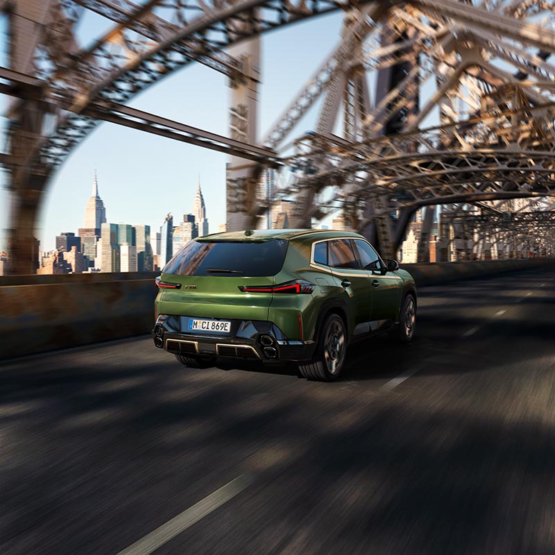 Grüner BMW XM fährt über eine Brücke – Dynamik und Leistung im Autohaus BMW Köhler in Karlstadt