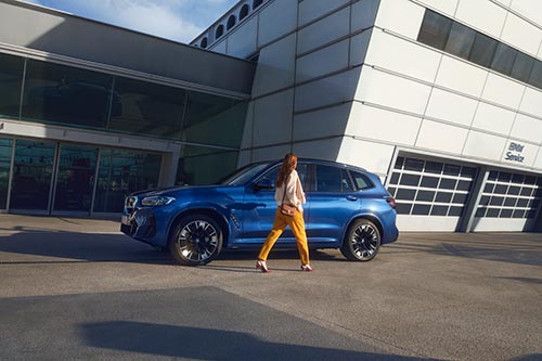 BMW iX3 vor einem modernen Gebäude und eienr Frau davor - Fortschritt und Design im Autohaus BMW Köhler in Karlstadt