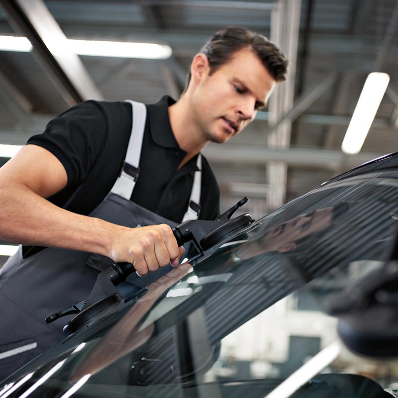 Mitarbeiter setzt die Windschutzscheibe eines BMW ein – Scheibenreparatur im Autohaus BMW Köhler in Karlstadt
