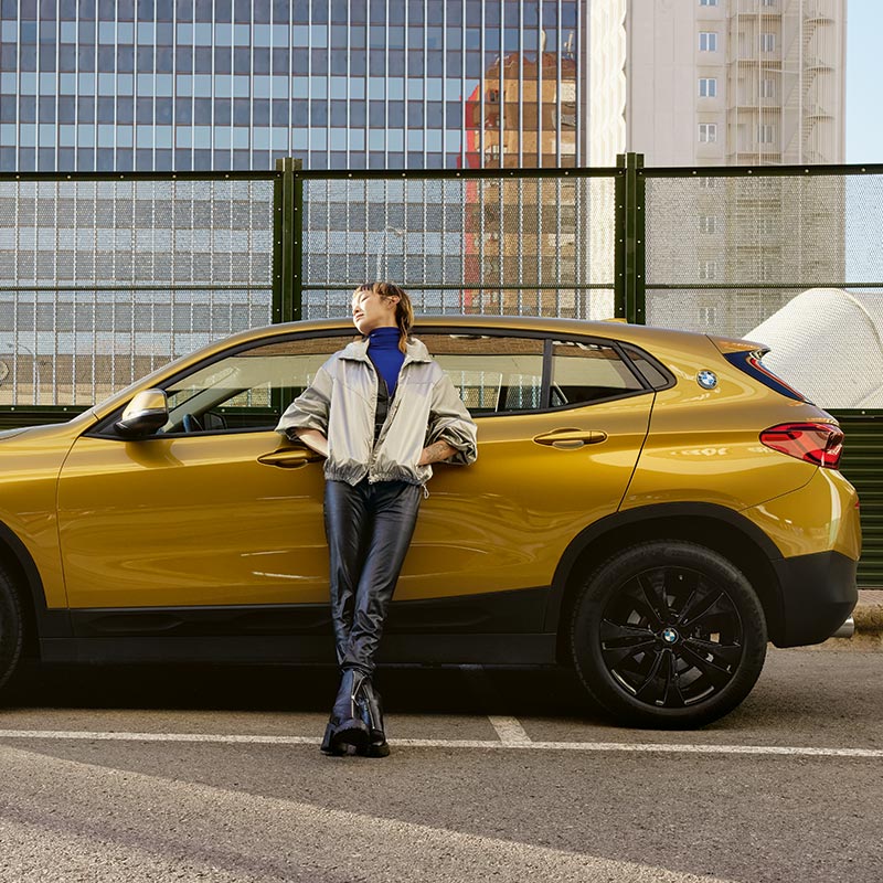 Mann lehnt an einem goldenen BMW X2 – Urbaner Lifestyle im Autohaus BMW Köhler in Karlstadt
