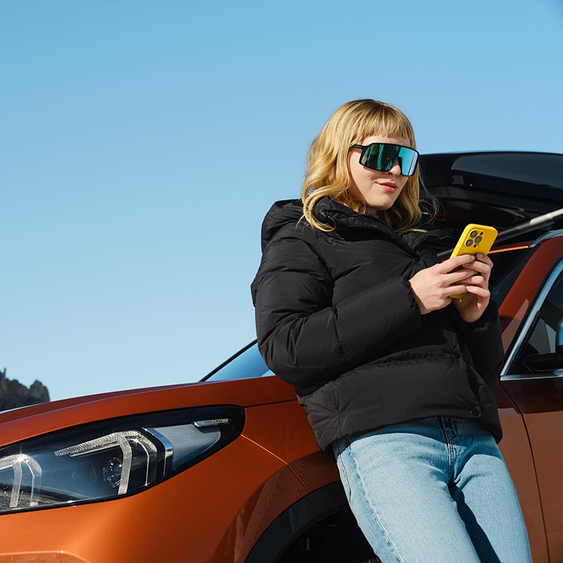 Frau mit Smartphone in der Nähe eines BMW – Moderne Technologie im Autohaus BMW Köhler in Karlstadt