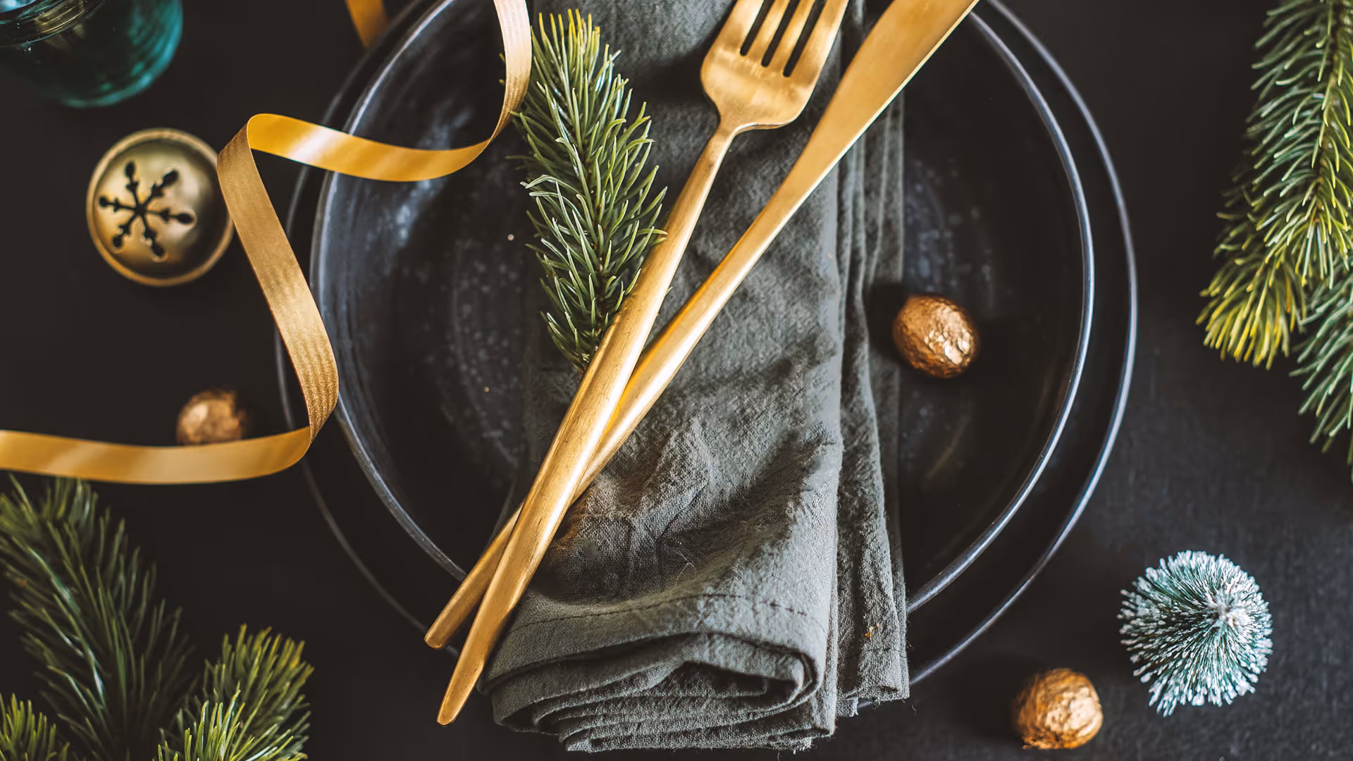 Festliche Tischdekoration mit goldenen Bestecken, Tannenzweigen und Band