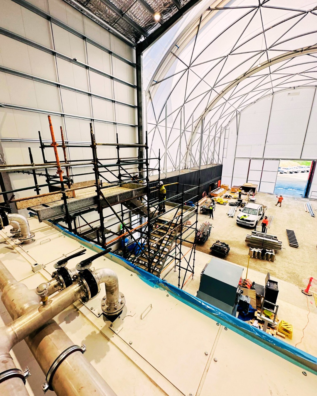 Construction worker in orange safety gear pouring cement onto a construction site with a detour sign and pedestrians in the background