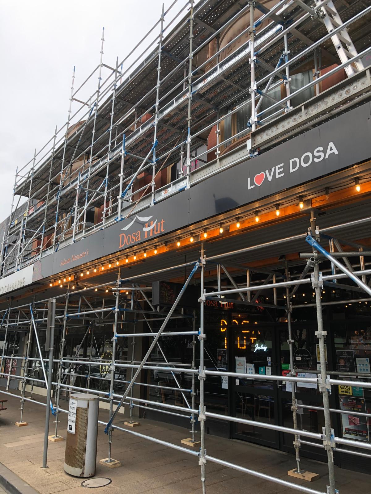 Restaurant storefront with mobile scaffolding surrounding it and signs reading 'Dosa Hut' and 'LOVE DOSA' above the entrance.