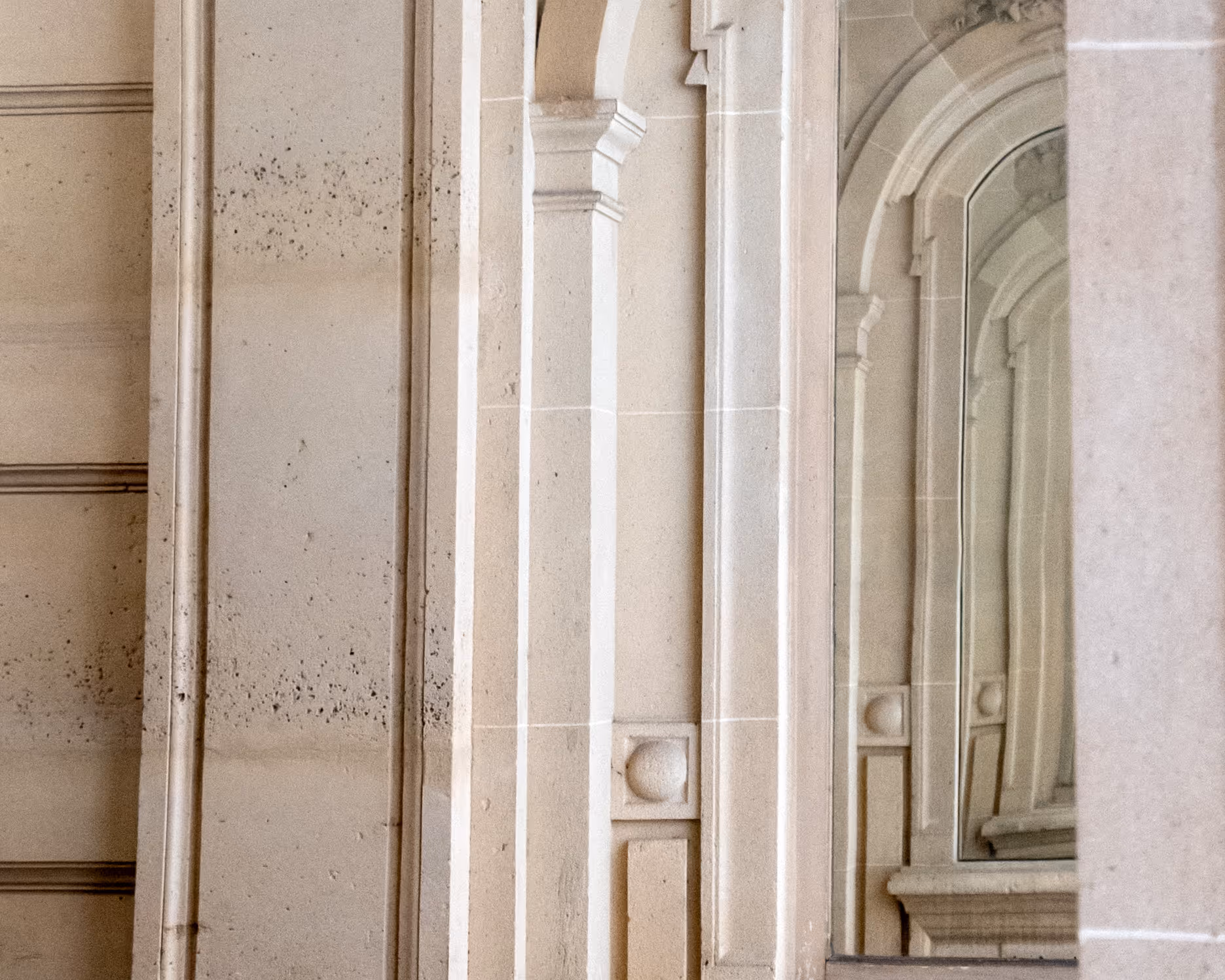 Colonne en pierre beige avec un grand miroir reflétant l'architecture ornée d'arcs.