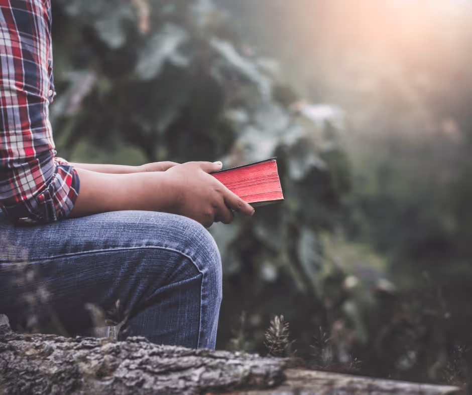 a man sits cross legged with a bible in his hands. His head is not visible and the sun is shining down