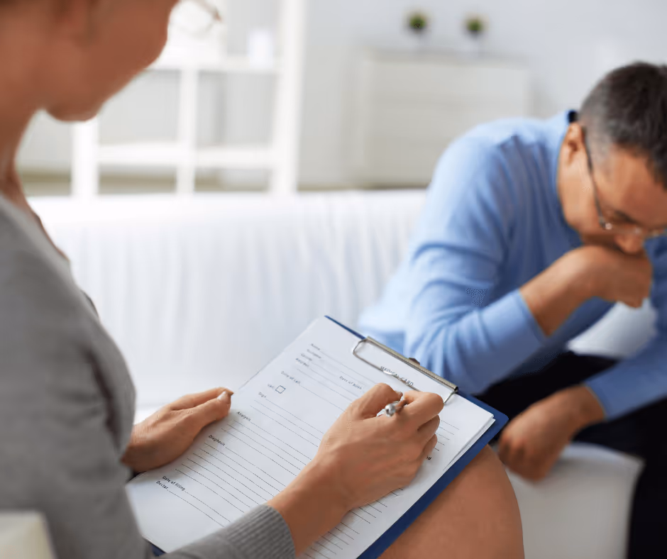 A man sitting with his head in his hands while a therapist is in the foreground