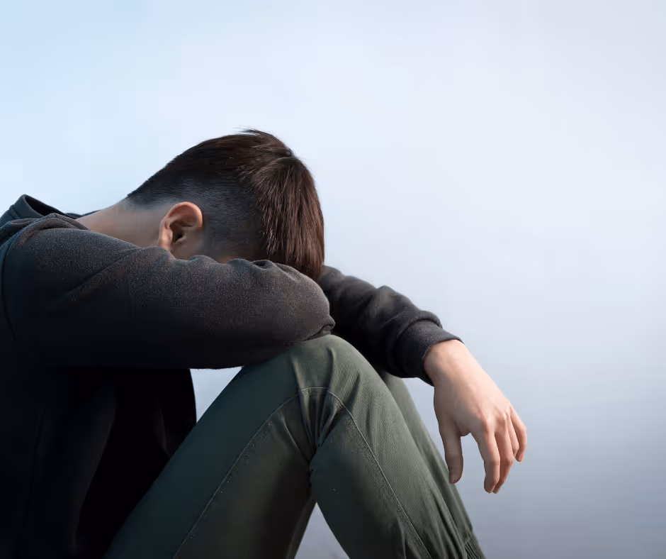 A man sits on the ground with his head down and leaning on his knees.