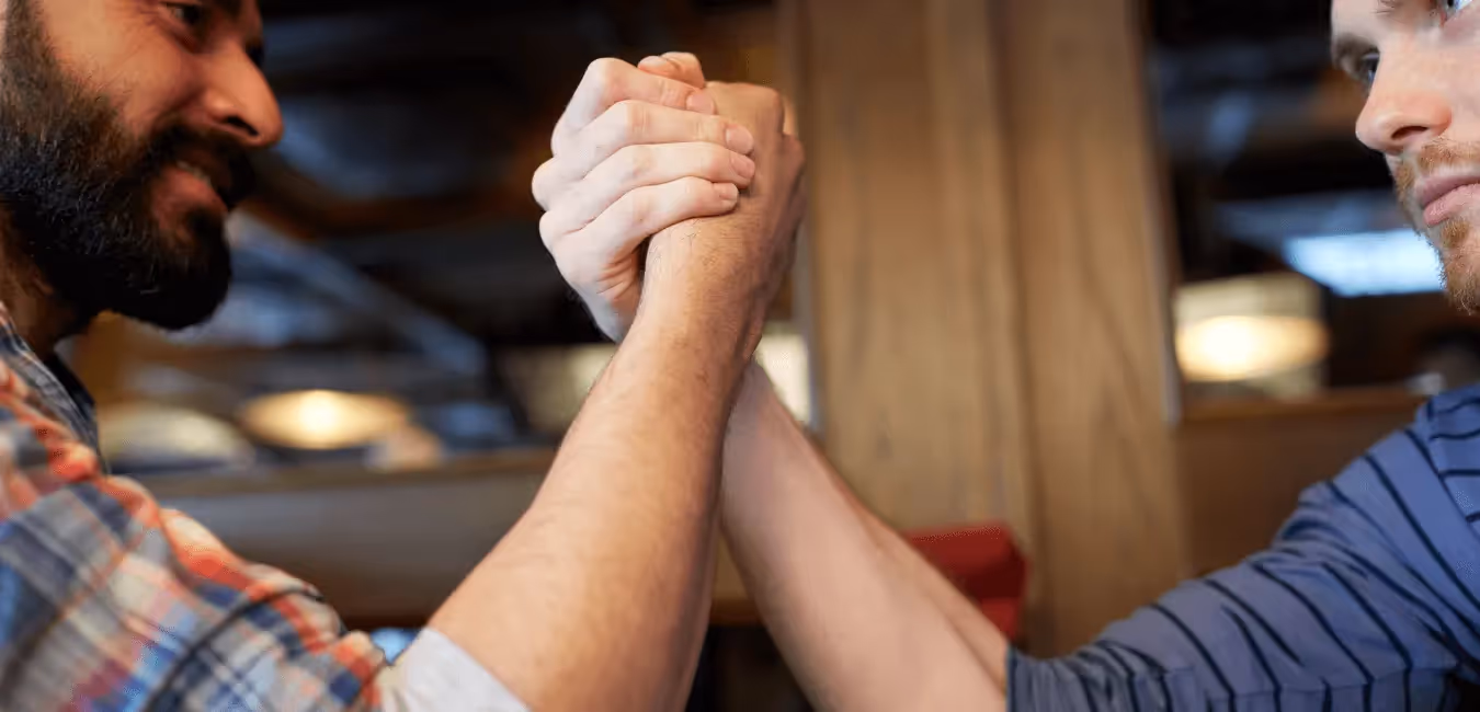 Close up of two men in a friendly arm wrestling at a table in a room