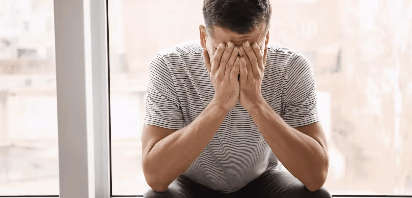 Young man sits near glass door, looking sad and crying.