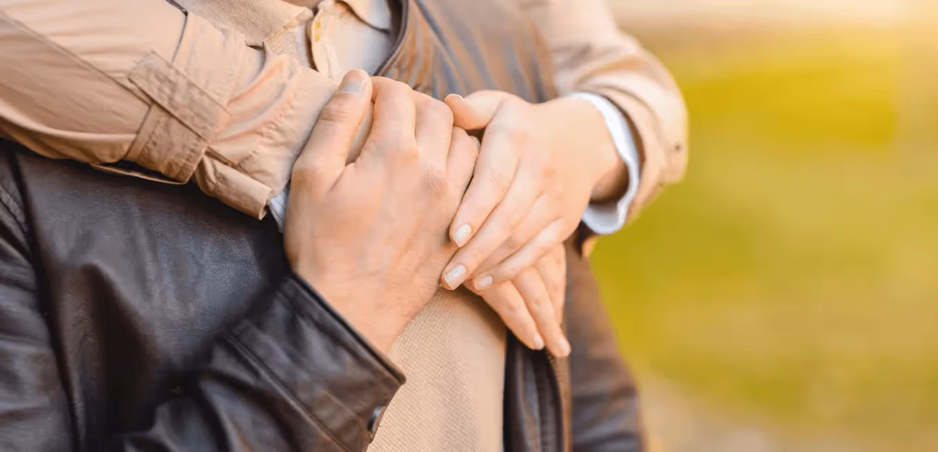 Woman wearing brown jacket hugging man wearing leather jacket from behind