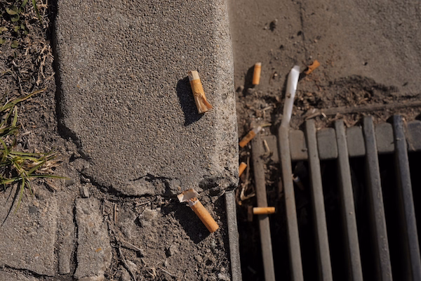 a cigarette butts on the ground next to a drain