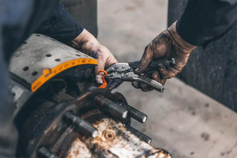 Technician performs brake repair using locking pliers near a worn rotor and marked brake pad.