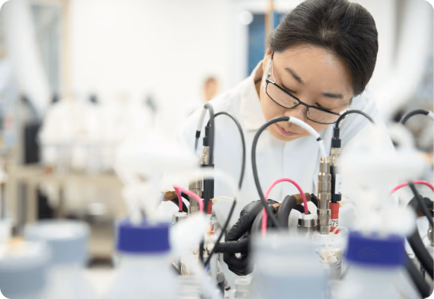 A woman wearing glasses and a white lab coat is working on a project. 