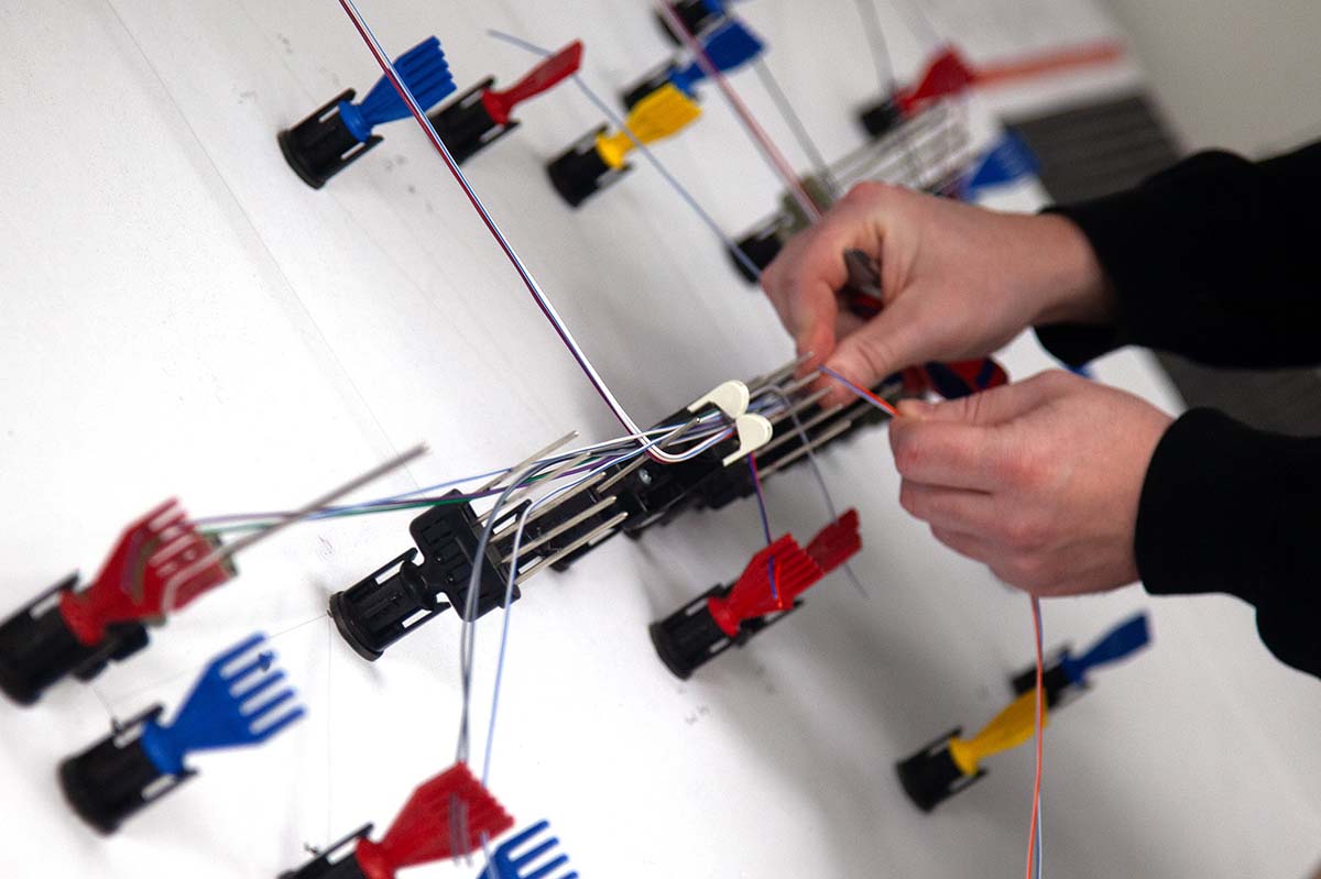 Technician assembling a custom wiring harness on a jig board, carefully routing coloured wires through layout guides to ensure accuracy and consistency across complex builds.
