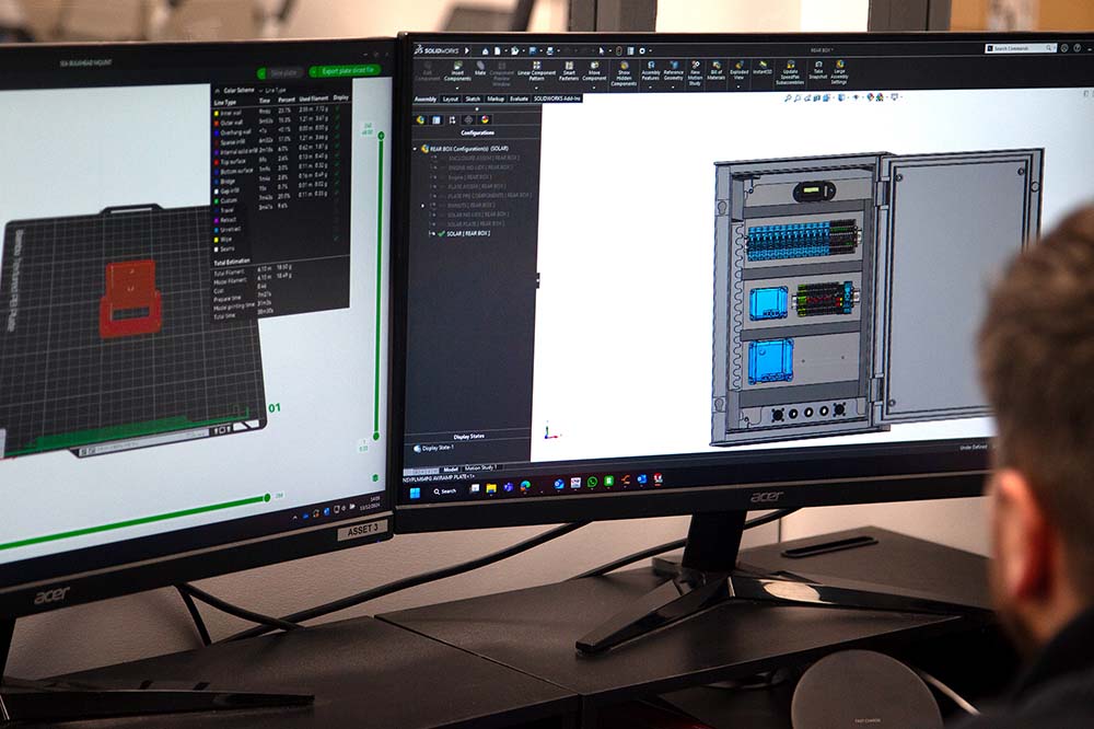 Dual-screen CAD setup showing a 3D model of a wiring control panel in design phase, illustrating Tec-Stop’s use of digital prototyping and detailed planning in their bespoke wiring solutions.