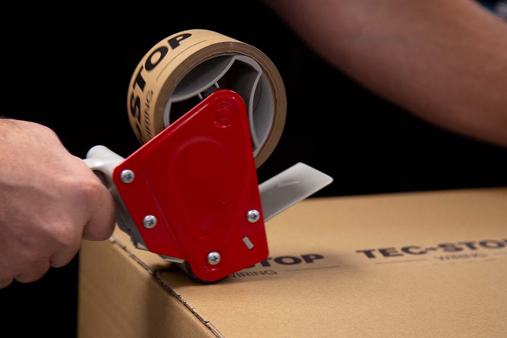 Close-up of a Tec-Stop team member sealing a branded box with custom packaging tape, preparing a wiring solution for dispatch.