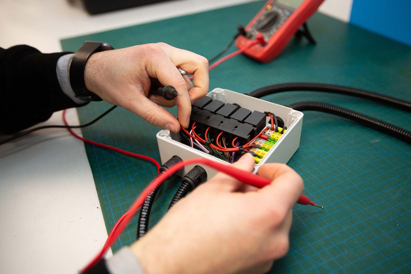 Tec-Stop technician testing electrical connections inside a completed control box using multimeter probes.