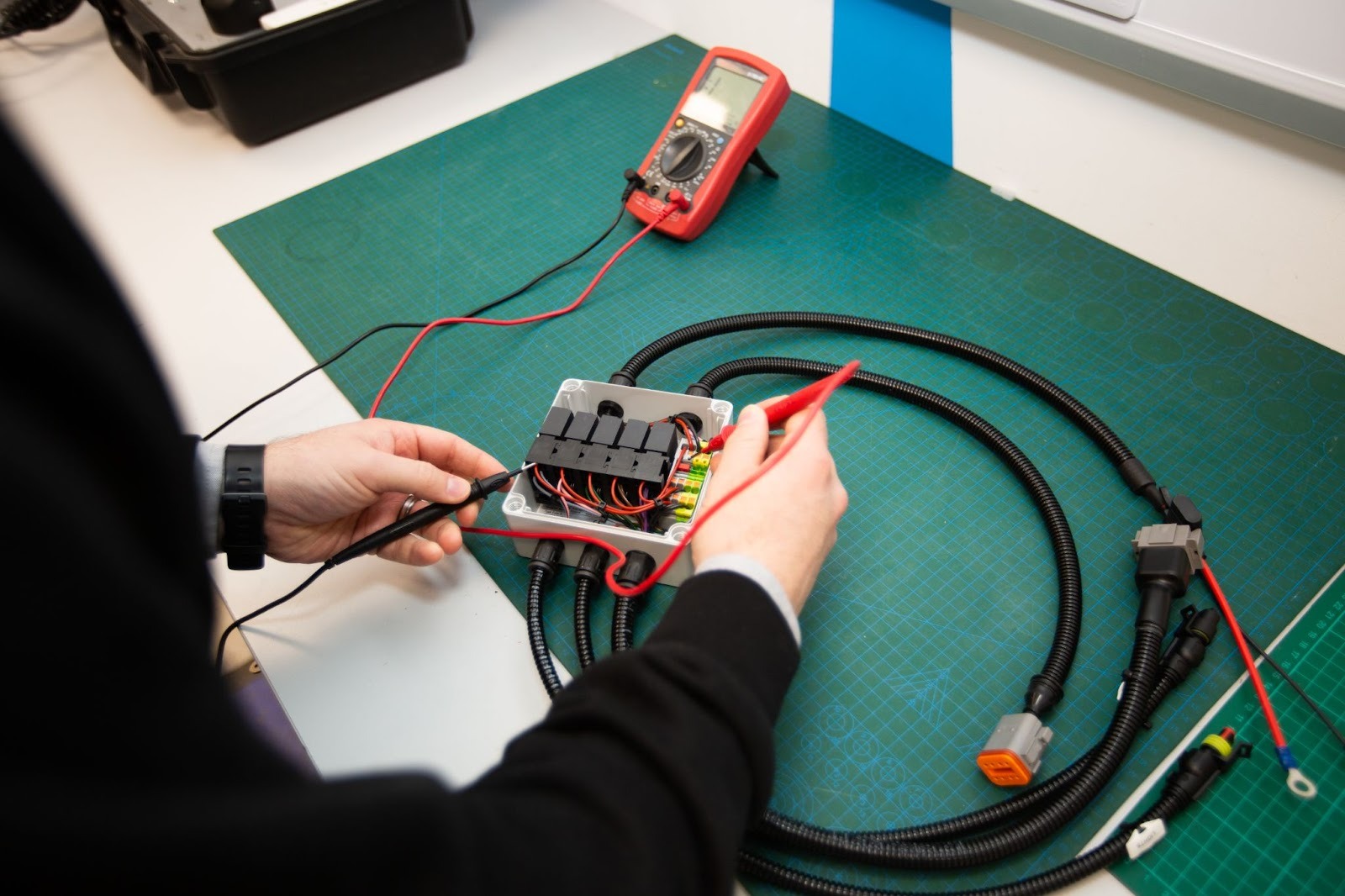 Tec Stop technician testing electrical wiring assembly using a multimeter during cable harness inspection