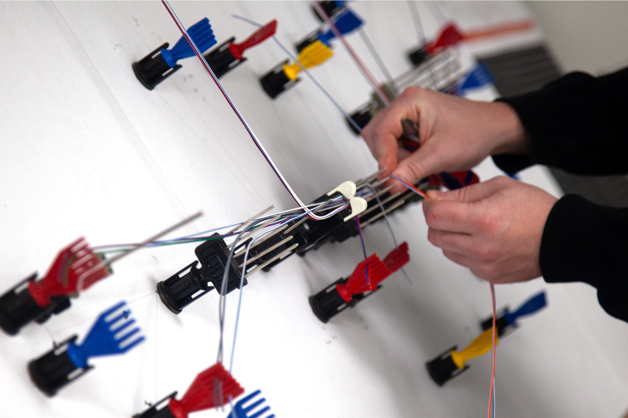 Technician assembling wiring harness on a layout board with wires, connectors and routing guides