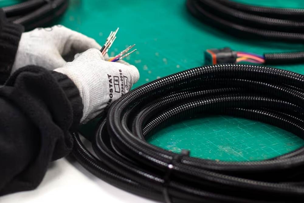 Technician assembling an automotive wiring harness with protective conduit and sleeving