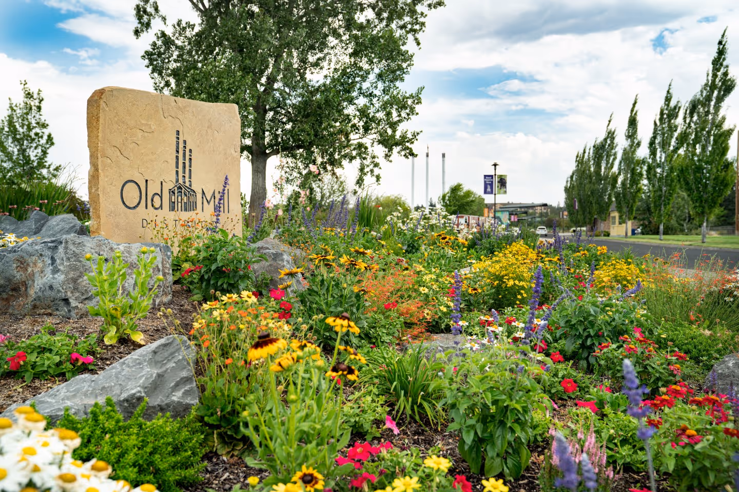 A manicured garden with colorful flowers, a green lawn, and a large engraved stone marker in the background.