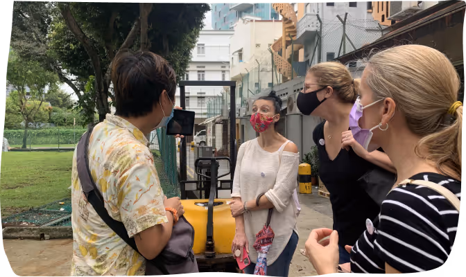 Four people wearing face masks engaged in conversation outdoors near a forklift and buildings.