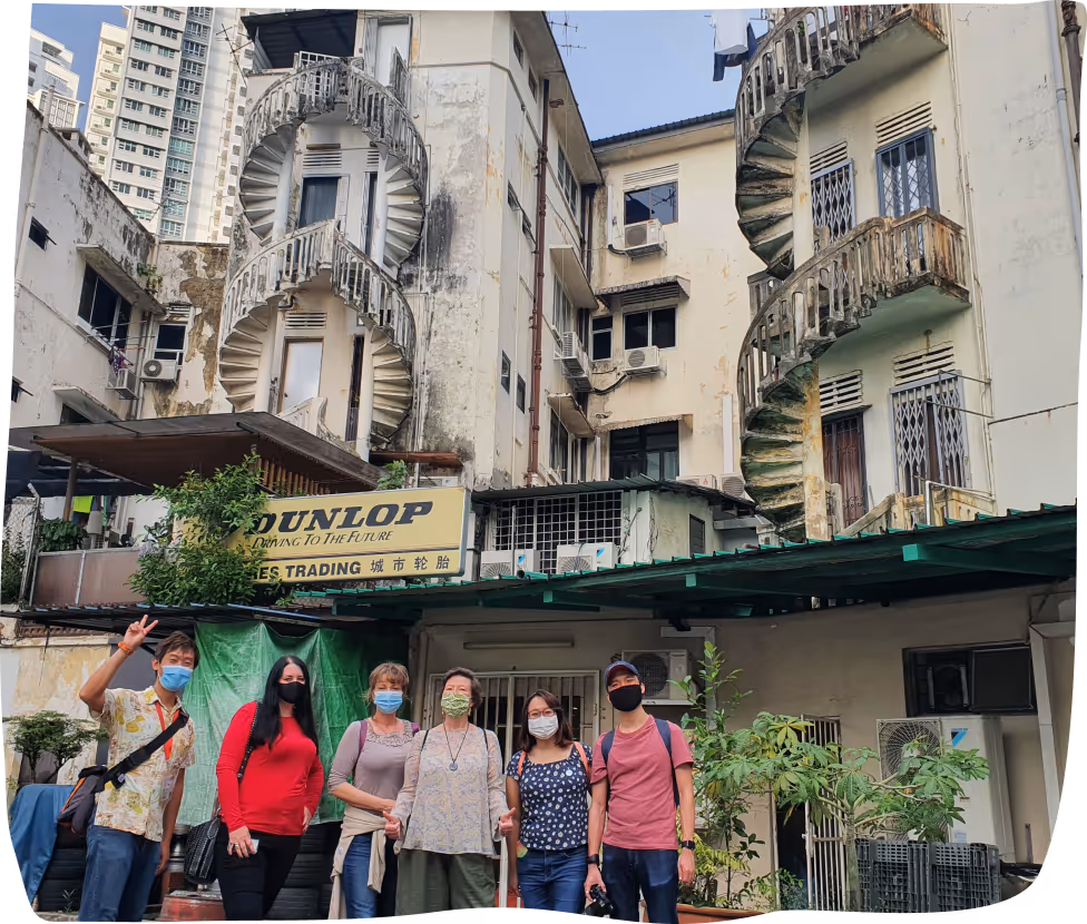 Group of six people wearing face masks standing in front of an old building with two spiral staircases and a Dunlop sign.