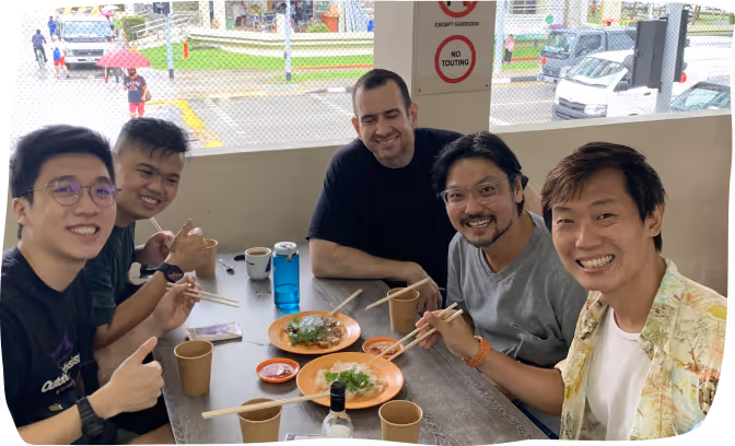 Five friends smiling and enjoying food together at a table with chopsticks and drinks.