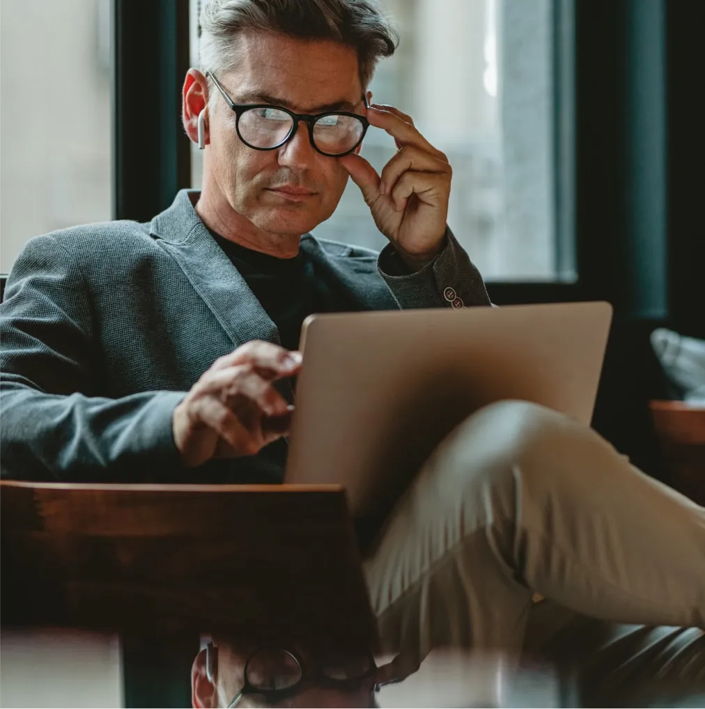 Hombre con gafas y auriculares, usando una laptop en un ambiente moderno y luminoso.