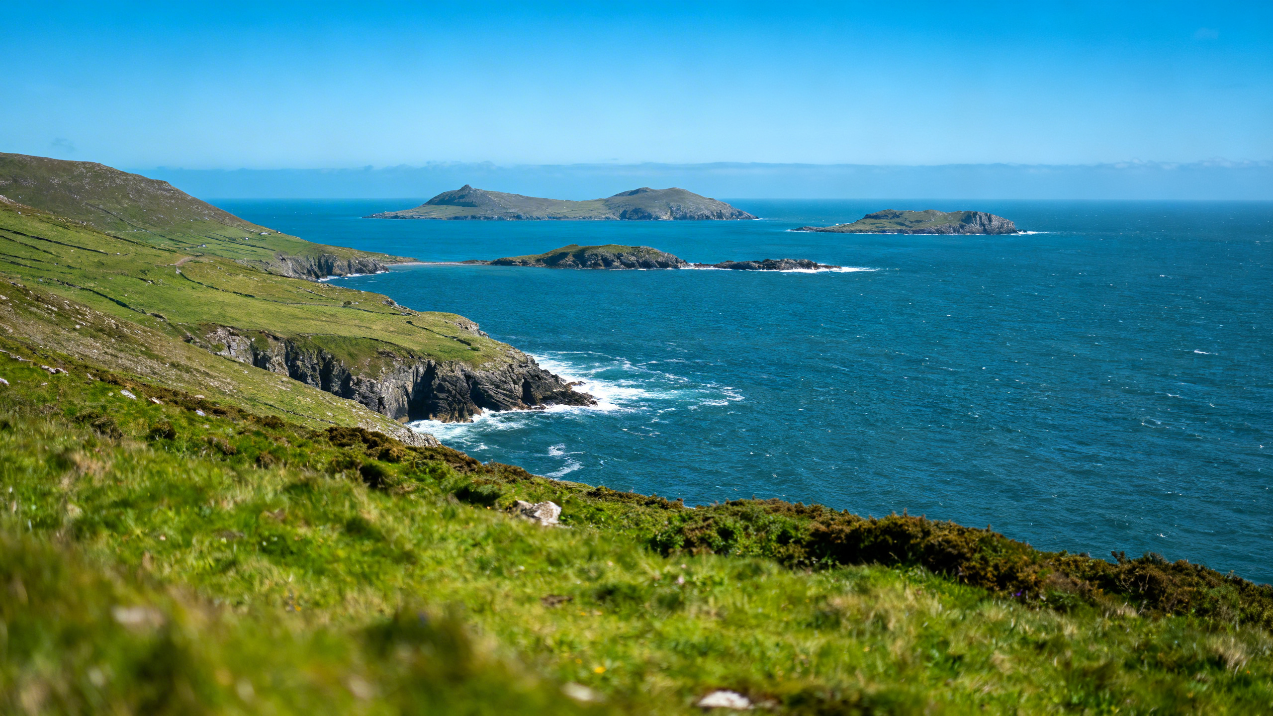 View south from the Slea Head Drive cliffside road, the Atlantic below, Blasket Islands visible across the sound, green headlands, clear sky