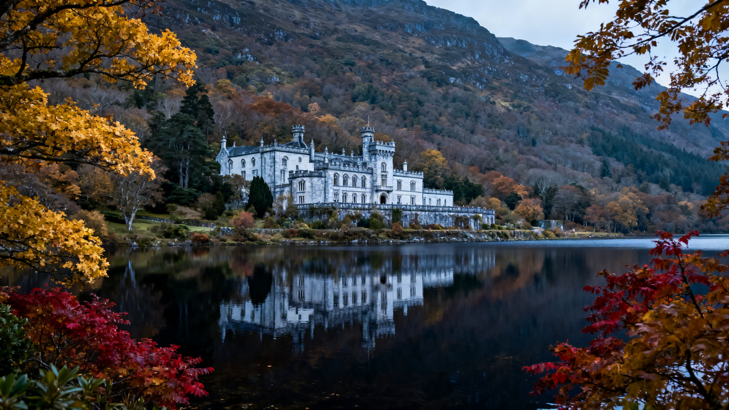 Kylemore Abbey reflected in the lake at its base, Victorian castle buildings against the wooded mountainside, calm water, soft overcast light