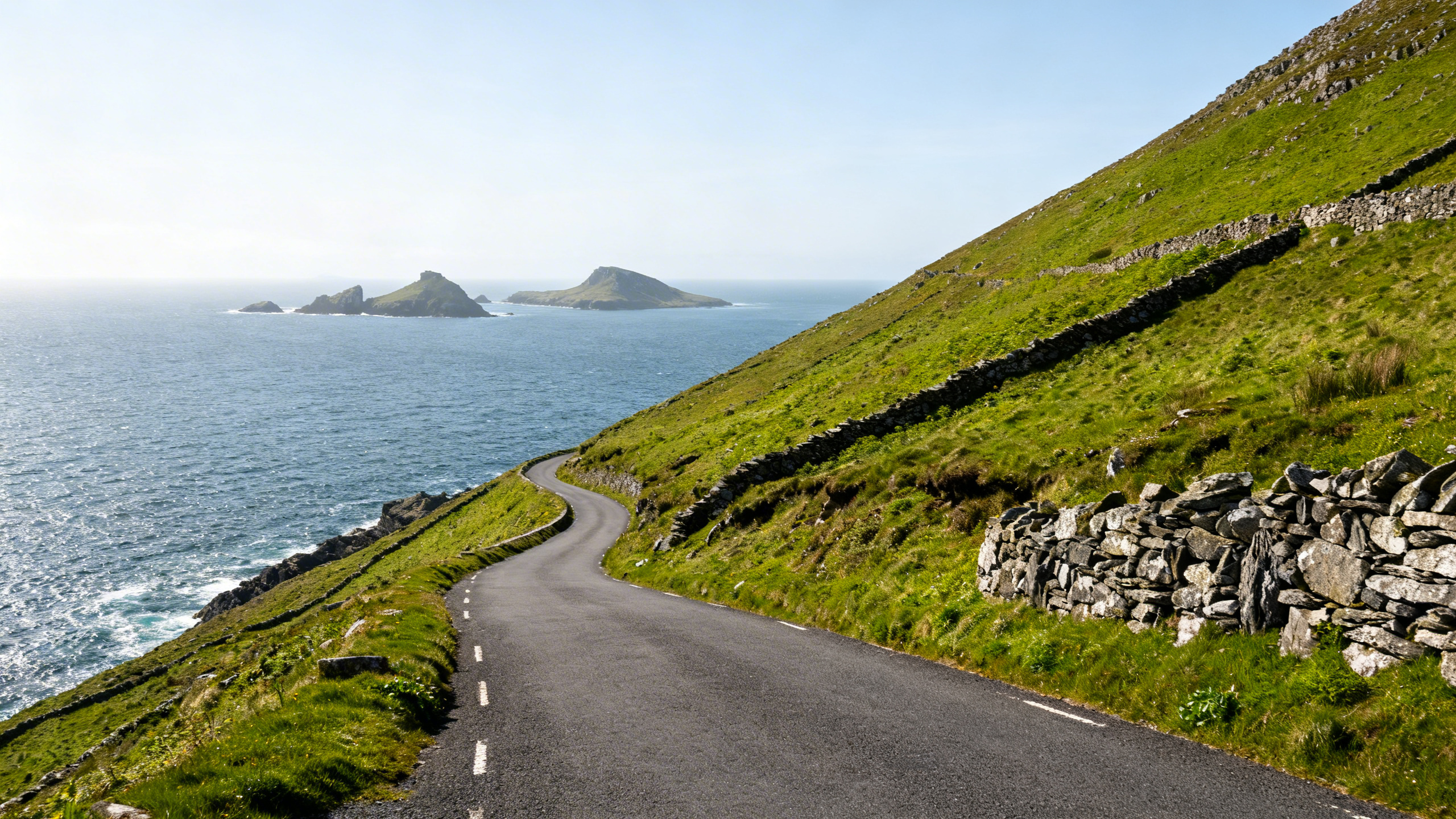 Slea Head Drive road switchbacking toward the sea with Blasket Islands visible in clear Atlantic light