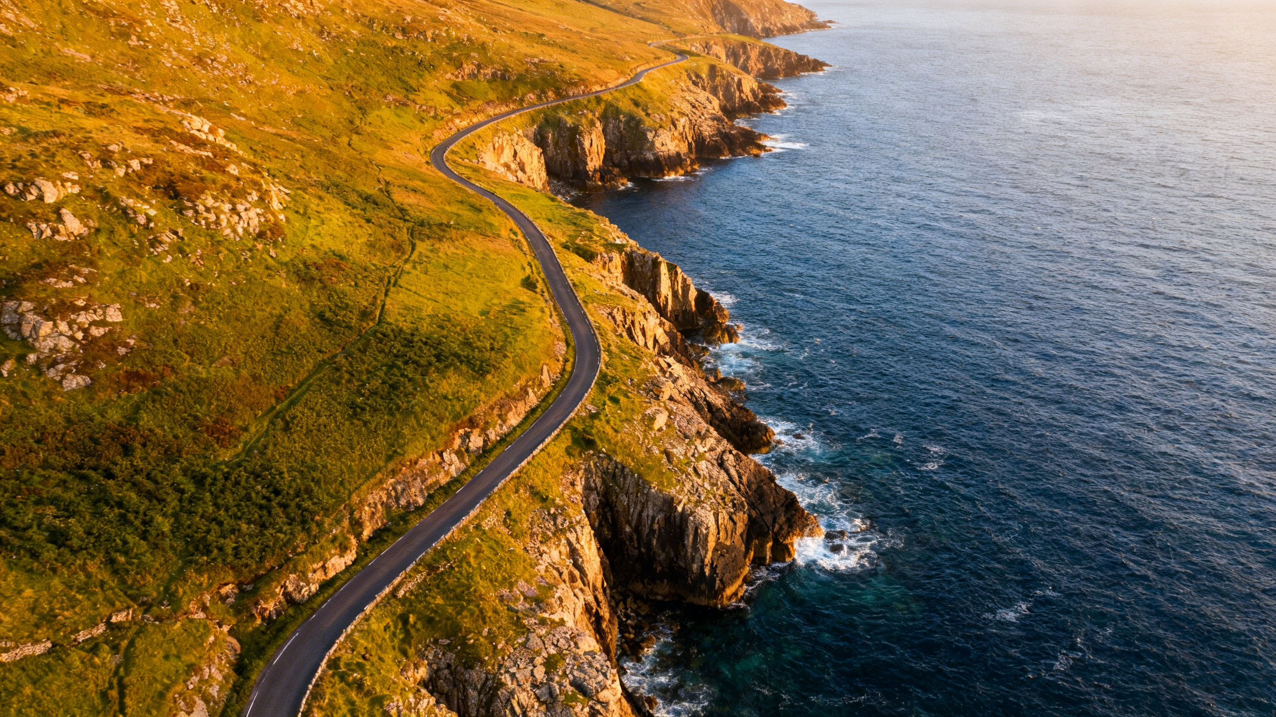 Winding coastal road in County Kerry at golden hour, viewed from above with Atlantic ocean and green headlands