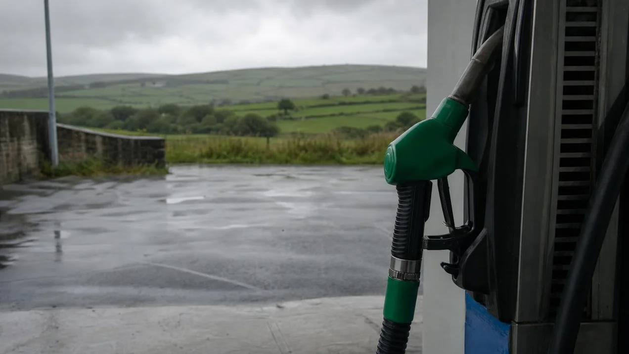 A fuel nozzle at an Irish petrol station, green fields visible beyond the forecourt. Overcast day, no people. Documentary style.