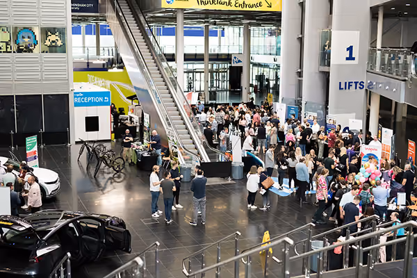 Crowds browsing stands, bikes and cars in a busy foyer at an employee wellness exhibition