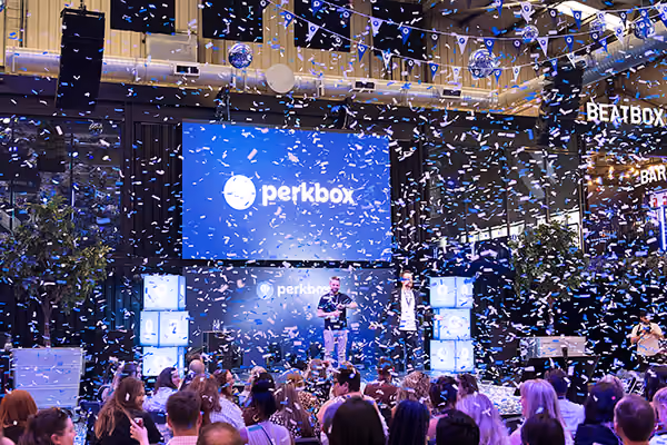 Confetti bursting over a crowd in front of a large branded screen at a company day