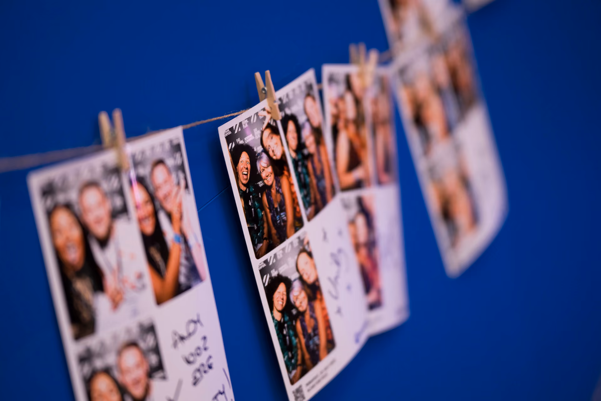 Photo booth strips pegged to a line against a blue wall at a company celebration
