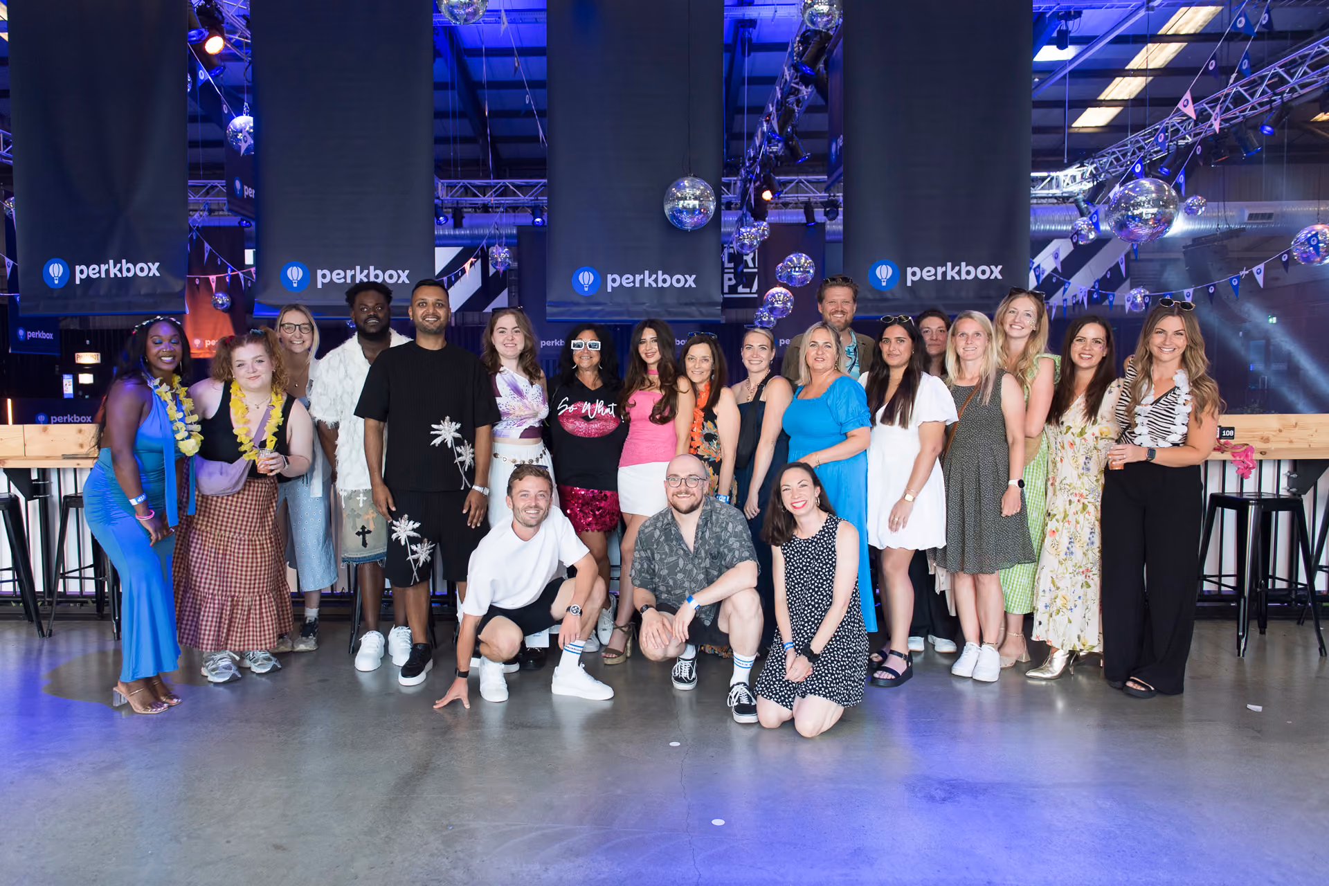 A large group of colleagues posing together in front of branded screens at a company party